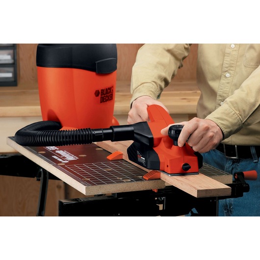 BLACKDECKER 7698K electric hand planer with dust hose in use on wooden board, close-up workspace view.