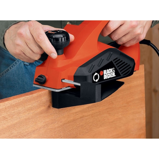 BLACKDECKER 7698K electric hand planer in use on a wooden board, close-up of tool and hands.