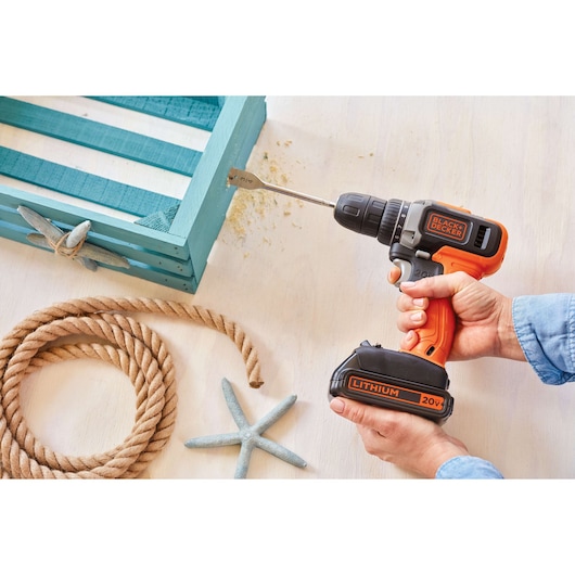 BLACK+DECKER BCD703C1 20V cordless drill in use on a teal wooden box, photography from top angle.
