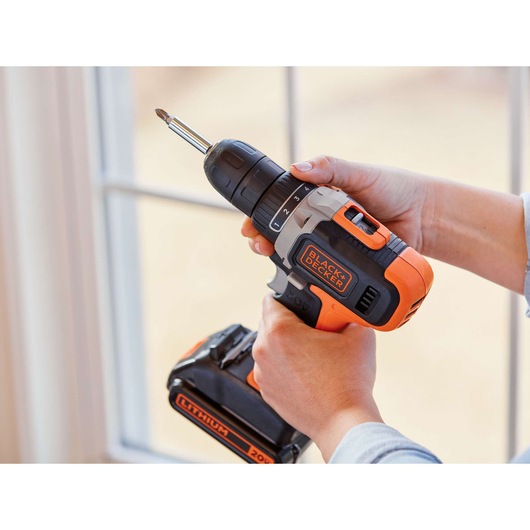BLACKDECKER BCD703C1 cordless drill with orange and black design, held in hand near window.