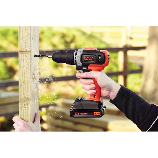 BLACKDECKER BCK21S1S cordless drill in use on wood, orange and black, 20V Lithium battery visible.