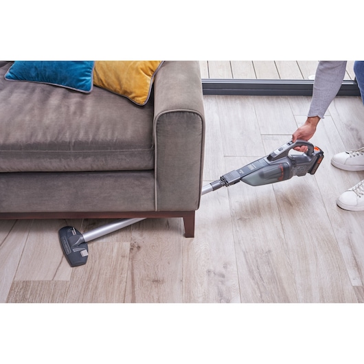 BLACKDECKER BCHV001D1 cordless stick vacuum cleaner cleaning under a sofa on wood floor, side angle.