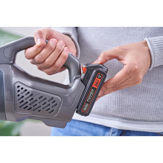 Photo of a person inserting BLACKDECKER 20V lithium battery, SKU BCHV001D1, into a handheld vacuum cleaner.
