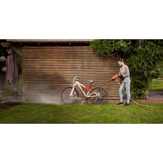 Photo of person cleaning a bicycle with BLACK+DECKER BCPC20D1 pressure washer outdoors.