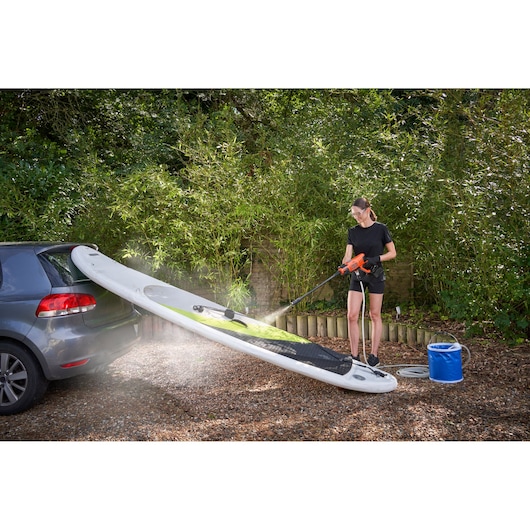 Photo of BLACKDECKER BCPC20D1 cordless pressure washer cleaning a paddleboard next to a parked car outdoors.
