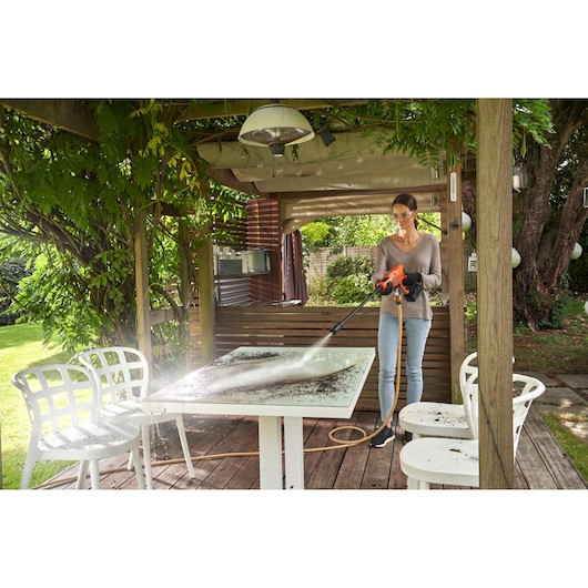 BLACKDECKER BCPC20D1 pressure washer cleaning outdoor table, shown in garden setting.