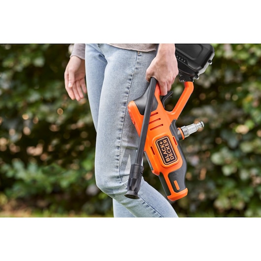 Photo of person holding BLACK+DECKER BCPC20D1 cordless orange pressure cleaner outdoors.