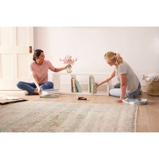 BLACKDECKER BCRTA601I cordless screwdriver on wooden floor near two people organizing books on white shelf.