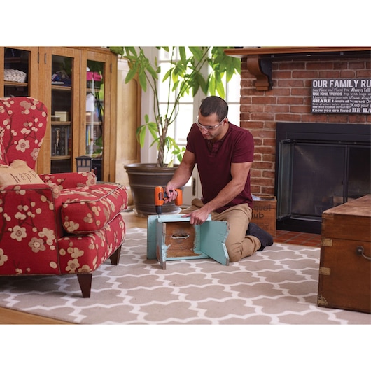 Photo of person using BLACKDECKER BDCD8C cordless drill to assemble wooden furniture on living room rug.