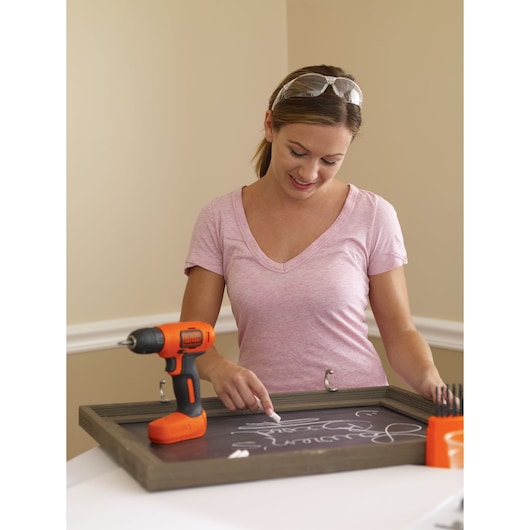 BLACKDECKER BDCD8C cordless drill on tabletop near woman writing on chalkboard, toolkit visible.