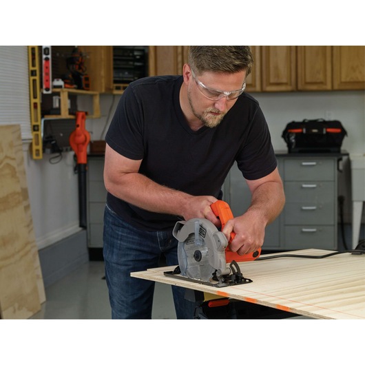 Photo of person using BLACK+DECKER circular saw BDECS300C to cut plywood in a workshop.