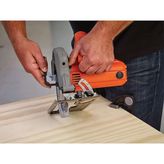 BLACKDECKER BDECS300C circular saw being adjusted on light wood, close-up angle showing orange and gray tool.