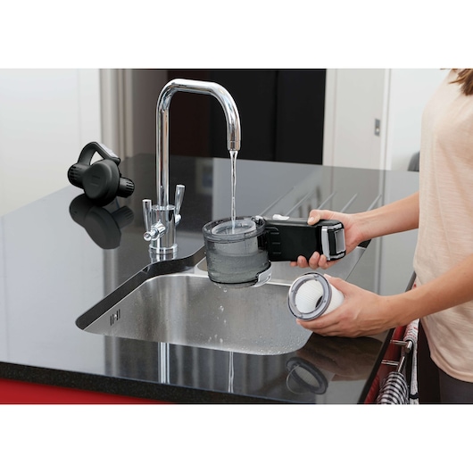BLACKDECKER BDH2000PL handheld vacuum filter being cleaned under running water at a kitchen sink.
