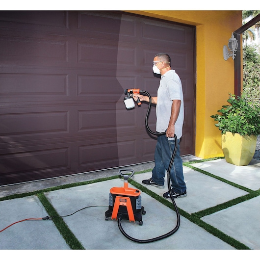 BLACKDECKER BDPH1200 paint sprayer used to paint a brown garage door outdoors.