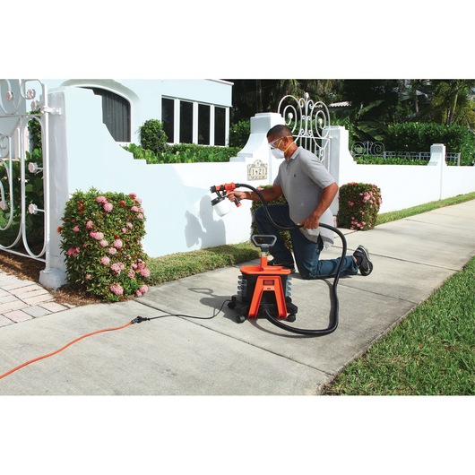 BLACKDECKER BDPH1200 paint sprayer in use painting a white wall outdoors, product with orange base visible.