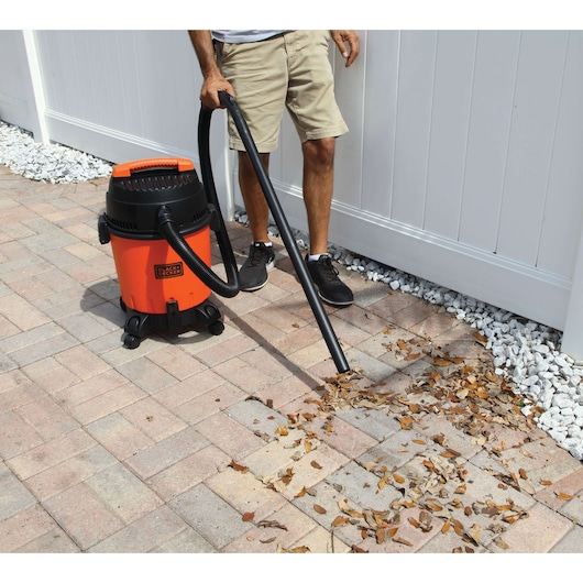 BLACKDECKER BDWD20 wet dry vacuum cleaning leaves on outdoor patio, user holding hose.