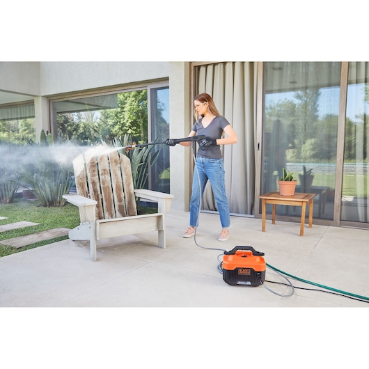 Photo of BLACKDECKER BEPW1600 pressure washer being used to clean a wooden chair on a patio.