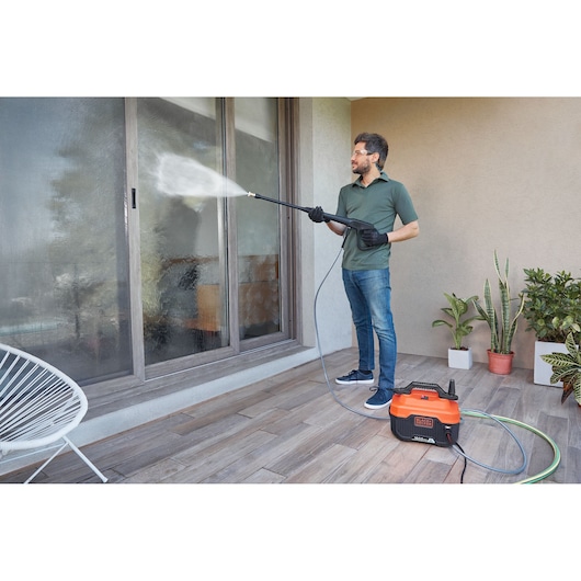 BLACKDECKER BEPW1600 pressure washer cleaning glass door on patio, person holding spray wand, plants in background.
