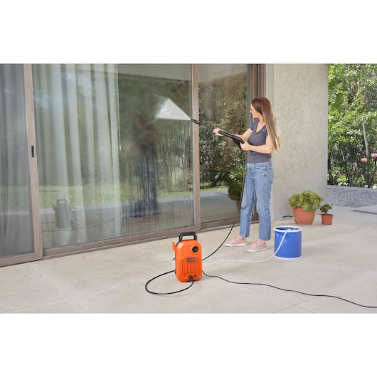 BLACKDECKER BEPW1600 pressure washer in use cleaning glass doors outdoors, product visible in orange.