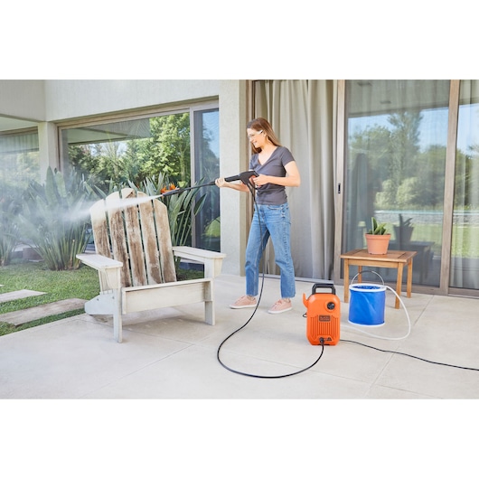 Photo of a person cleaning a wooden chair with BLACKDECKER BEPW1600 pressure washer outdoors on a patio.