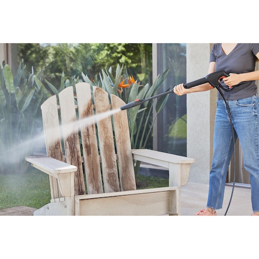 Person using BLACKDECKER BEPW1600 pressure washer to clean a dirty wooden outdoor chair.