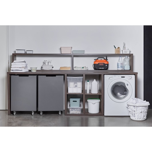 BLACKDECKER BEPW1600 pressure washer on laundry shelf with cleaning supplies, storage bins, and washing machine, straight angle.
