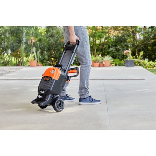 Photo of BLACKDECKER BEPW2200 pressure washer being wheeled outdoors by a person, showing portable design.
