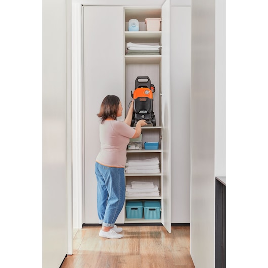 BLACKDECKER BEPW2200 pressure washer stored on a shelf in a white closet with folded towels and baskets.