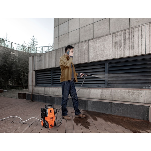 BLACKDECKER BEPWB1740 pressure washer in use cleaning outdoor wall, orange and black unit on wood deck.
