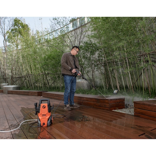 BLACKDECKER BEPWB1740 pressure washer cleaning wooden deck outdoors, orange unit visible in foreground.