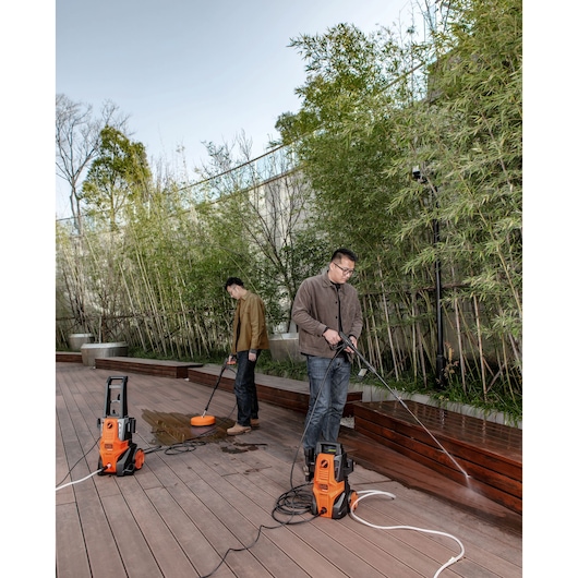 Two people using BLACKDECKER BEPWB2000 pressure washers to clean outdoor wooden decking in a garden setting.
