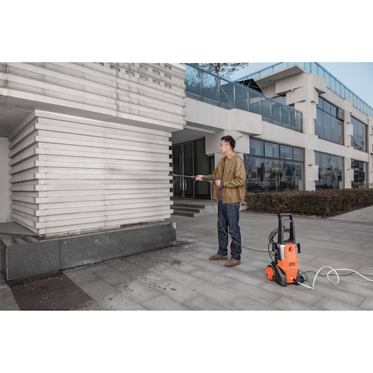 BLACKDECKER BEPWB2000 pressure washer cleaning exterior wall, orange unit on pavement, outdoor setting.