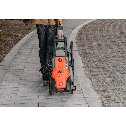 Photo of BLACKDECKER BEPWB2000 pressure washer being pulled on pavement by person, orange and black design.