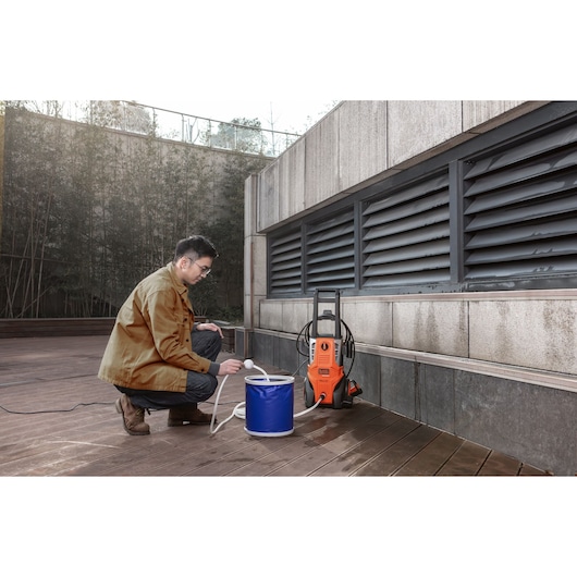 BLACKDECKER BEPWB2000 pressure washer in use outdoors, with blue water bucket, man connecting hose.
