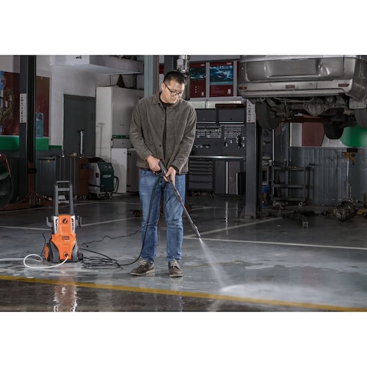 BLACKDECKER BEPWB2000 pressure washer in use cleaning garage floor, person holding spray wand, indoor setting.