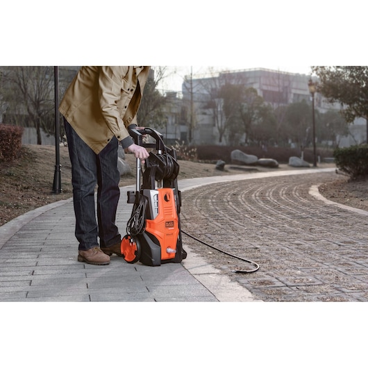 BLACKDECKER BEPWB2400 pressure washer on a paved walkway outdoors, held by person in casual clothing.