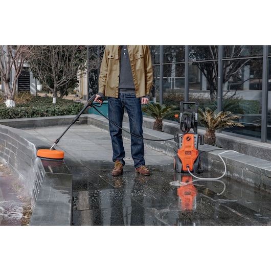 BLACKDECKER BEPWB2400 pressure washer cleaning outdoor pavement, orange unit with hose and surface cleaner.