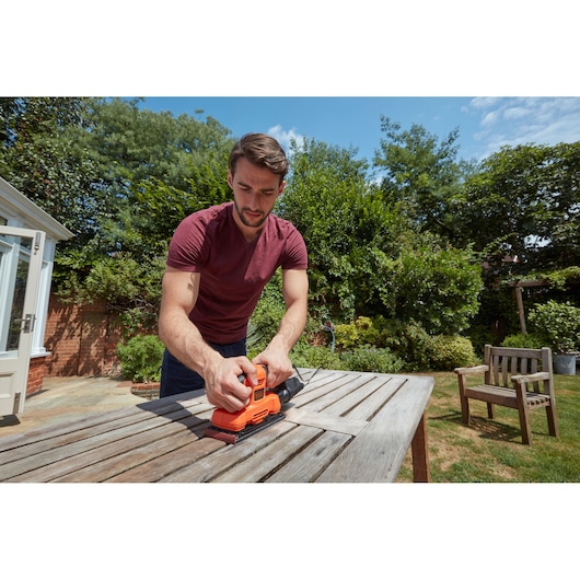 BLACKDECKER BEW220 sander used on wooden outdoor table in garden setting.