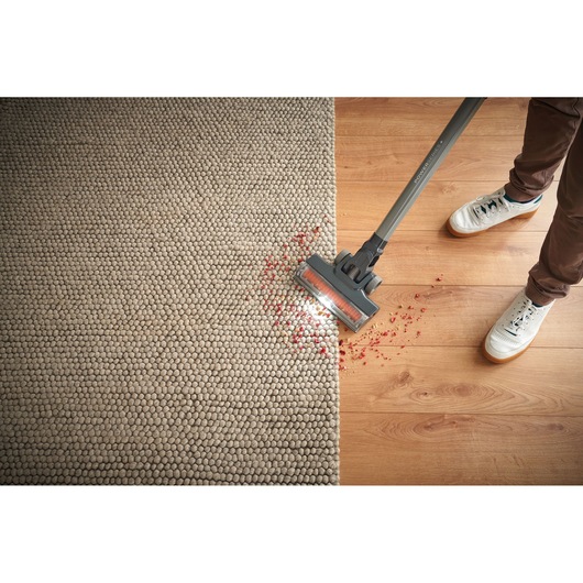 BLACKDECKER BHFEA18D1 cordless stick vacuum cleaning red debris from rug and hardwood floor, top-down view.