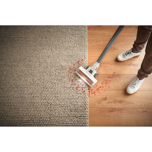 BLACKDECKER BHFEA520J cordless stick vacuum cleaning red debris from carpet and hardwood floor, top view.