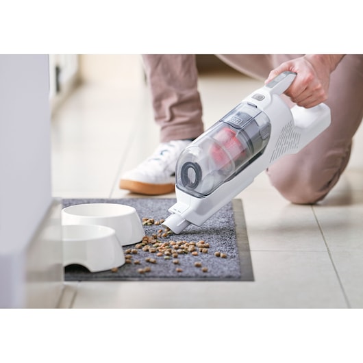 BLACKDECKER BHFEA520J handheld vacuum cleaning pet food from mat near white bowls, close-up angle.