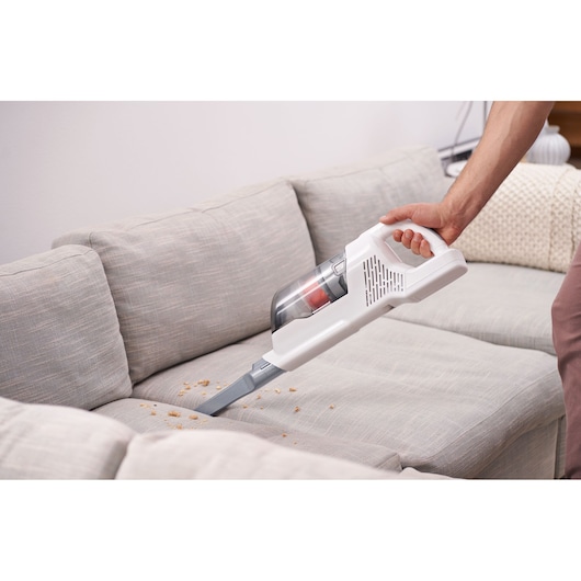 BLACKDECKER BHFEA520J handheld vacuum cleaner with long nozzle cleaning crumbs on a light gray sofa.