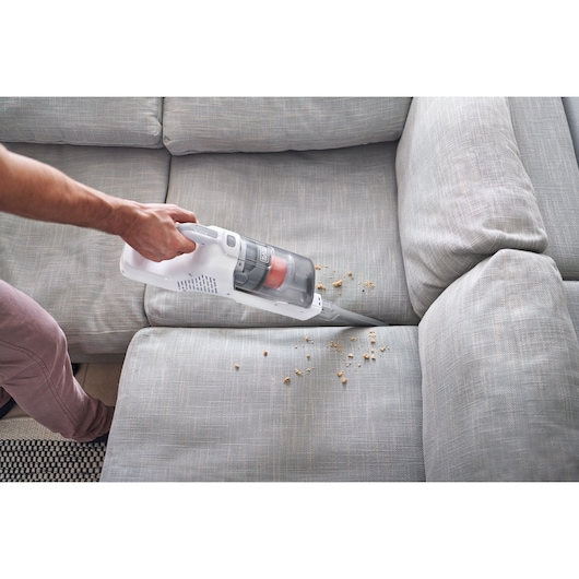 BLACK+DECKER BHFEA520J cordless handheld vacuum cleaning crumbs from a gray sofa crevice.