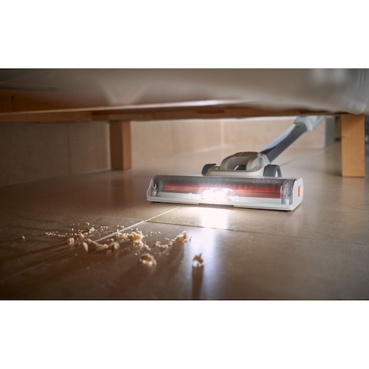BLACKDECKER BHFEA520J cordless stick vacuum cleaning crumbs under furniture, close-up view with floor lighting.