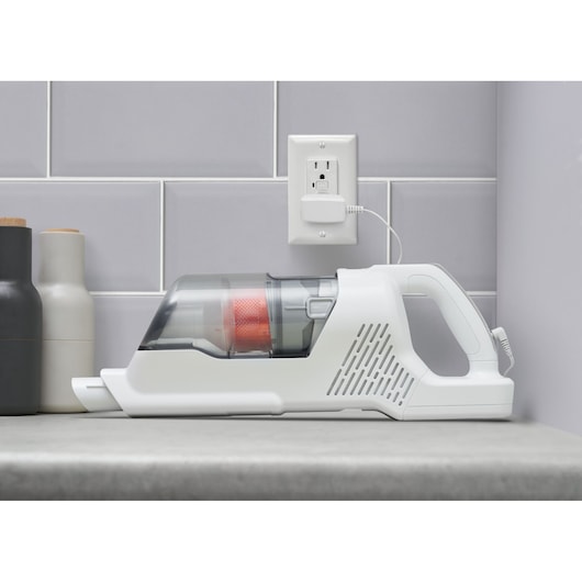 BLACKDECKER BHFEA520J handheld vacuum cleaner with white and gray body on a countertop, charging by wall outlet.
