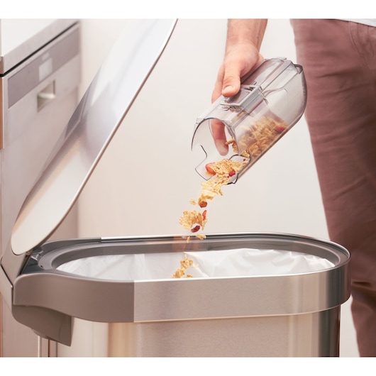 BLACKDECKER BHFEA520J vacuum dustbin emptying debris into kitchen trash can, close-up view.
