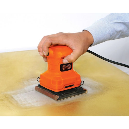 BLACKDECKER BS200 orange palm sander in use on a wooden surface, close-up angle.