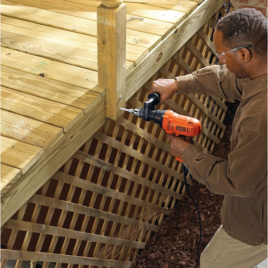 Photo of person using BLACKDECKER DR560 corded drill to fasten a screw into a wooden deck post outdoors.