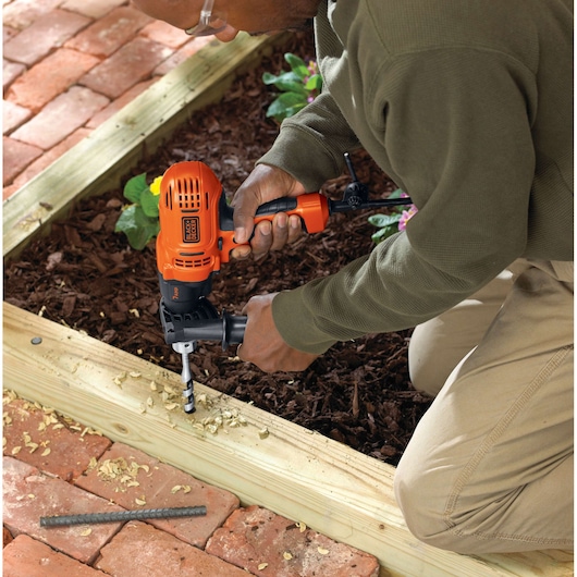 Photo of BLACKDECKER DR560 corded drill in use, drilling into exterior wooden frame in garden setting.