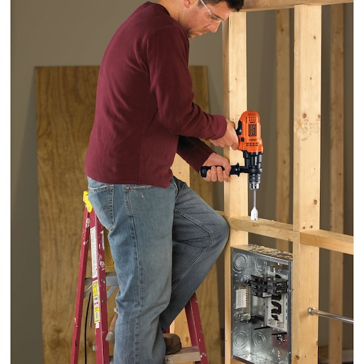 Photo of a person using BLACKDECKER DR560 electric drill on wood framing at construction site.